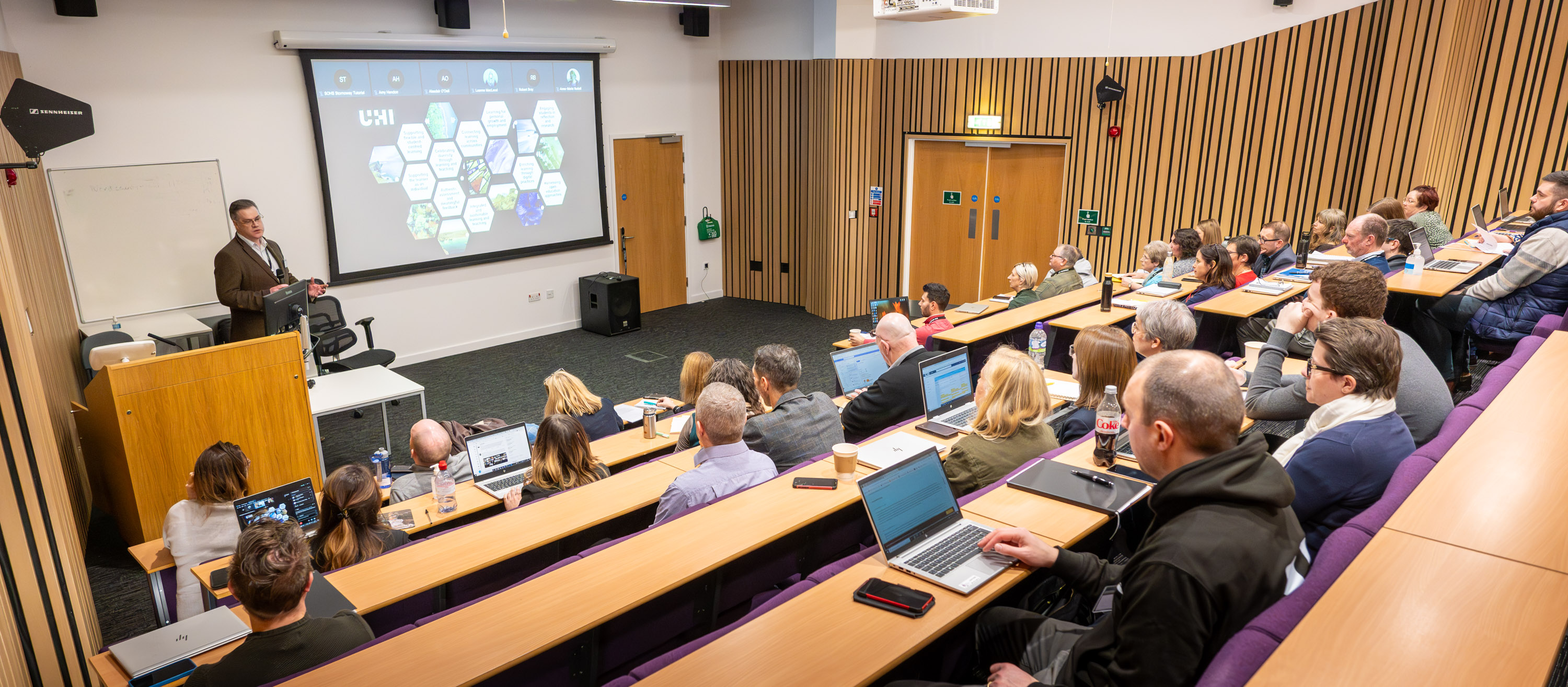 People in a lecture theatre listening to a lecturer People in a lecture theatre listening to a lecturer